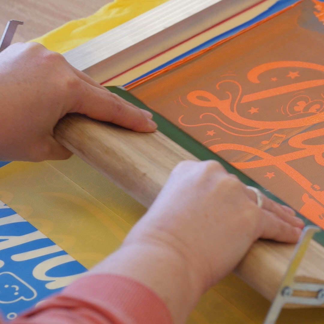 Siedruck Set DIY. Nahaufnahme von Händen, die einen Siebdruck in einem Siebdruckrahmen mit einer Siebdruckrakel ausführen.