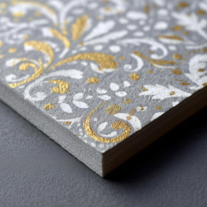 Closeup of a piece of thick cardboard screen printed with gold and white floral design.